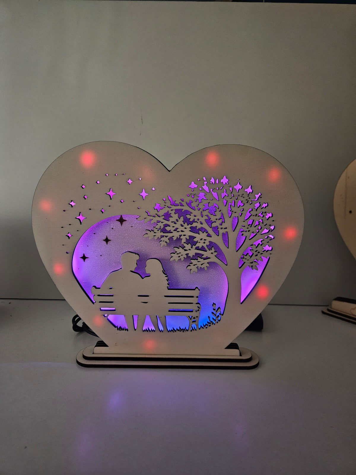 Holzherz mit RGB-LED-Beleuchtung und einem Paar auf einer Bank unter einem Baum